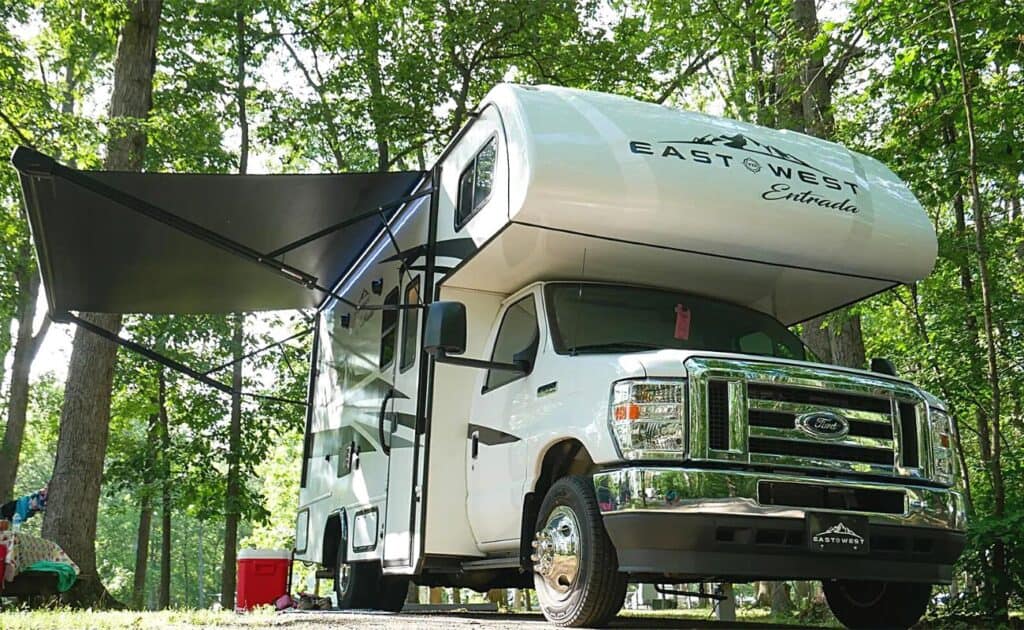 Class C motorhome, with an "East to West Entrada" Logo, Parked in a Lush, Wooded Campsite