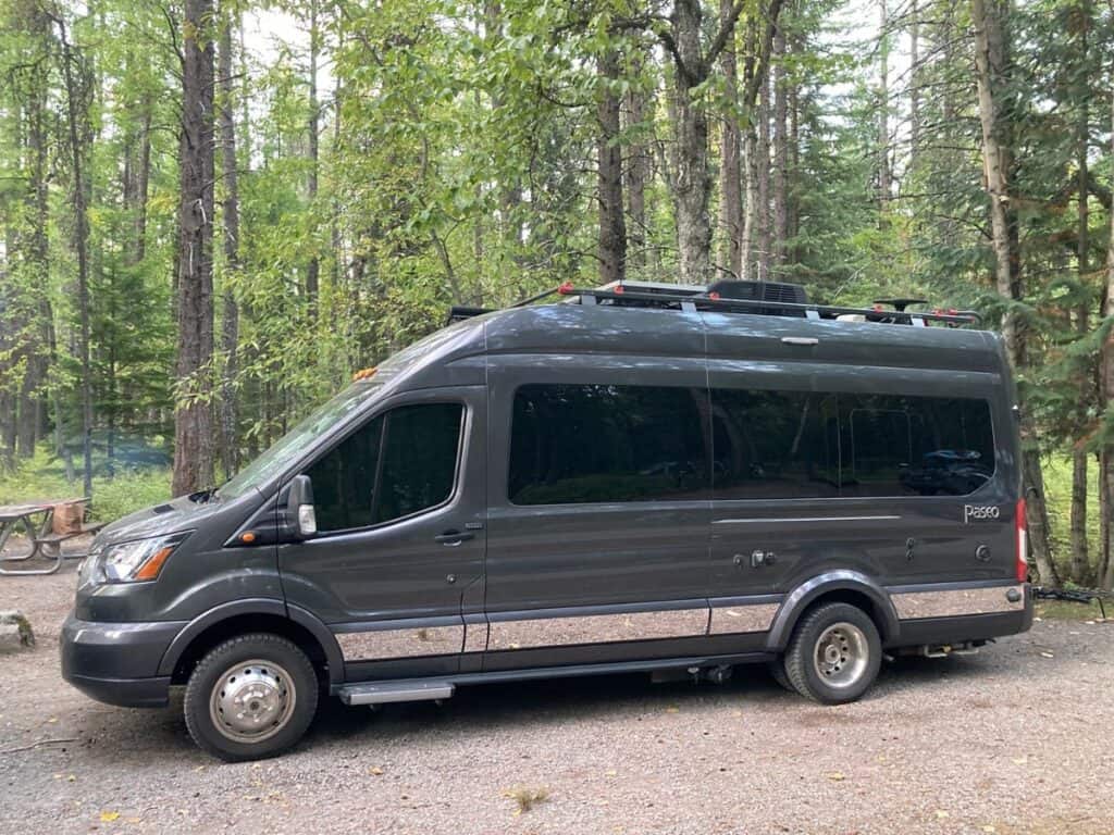 Dark Grey Class B RV Parked in a Serene, Wooded Campsite Surrounded by Tall Trees
