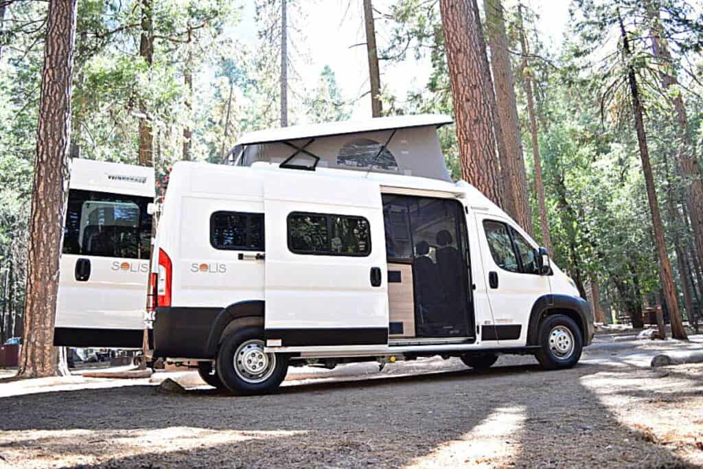 Winnebago Solis Class B RV with a Pop-top Roof Parked in a Forested Campground with Tall Pine Trees