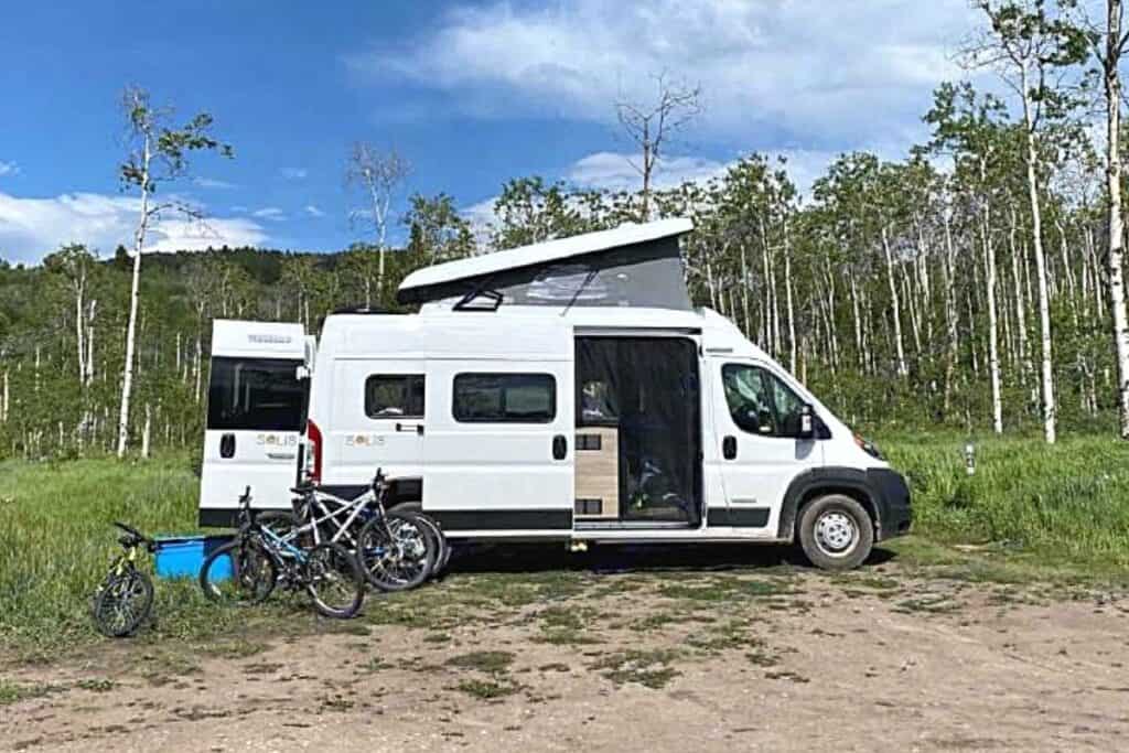 Class B Motorhome with a Pop-top Roof Parked in a Clearing Among a Stand of Aspen Trees Surrounded by Bicycles and Camping Gear