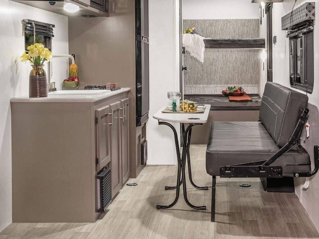 The Interior of the KZ RV Sportsmen Classic 180TH, featuring a kitchenette with modern appliances and wooden cabinetry, complemented by a booth-style dining area with a pedestal table and cushioned bench seating.