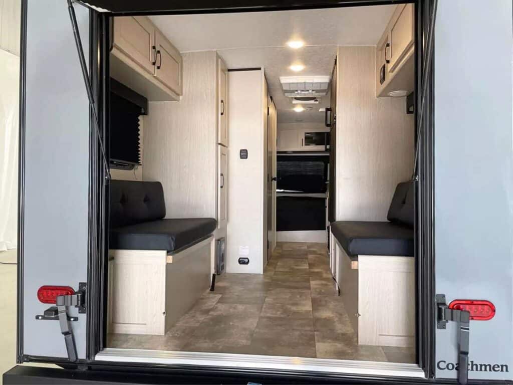 Looking through the rear entry hatch of the Coachmen Apex Nano 17TH, the interior is visible with bench seating on either side, overhead cabinets, and a central aisle leading towards additional living space.